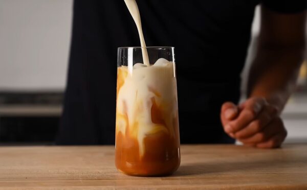 Yeung pours oat milk into the glass of vegan Thai tea