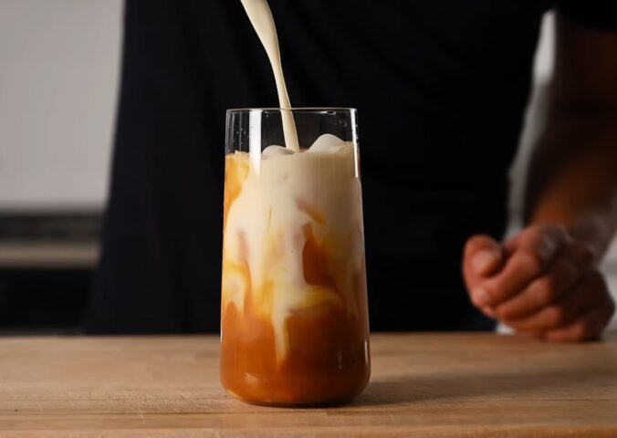 Yeung pours oat milk into the glass of vegan Thai tea