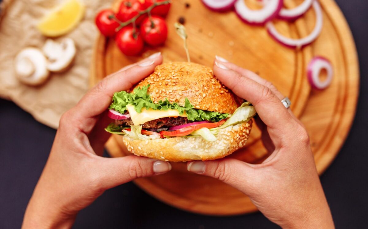 Photo shows a woman's hands holding a mushroom burger with a wooden chopping board and ingredients in the background. A new study has found that generative AI can help create more delicious, sustainable, and nutritious burgers, including plant-based options.