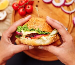 Photo shows a woman's hands holding a mushroom burger with a wooden chopping board and ingredients in the background. A new study has found that generative AI can help create more delicious, sustainable, and nutritious burgers, including plant-based options.