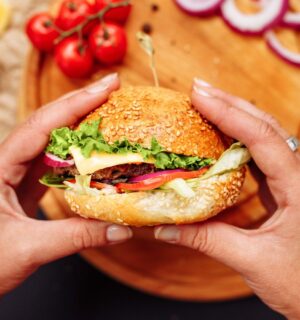 Photo shows a woman's hands holding a mushroom burger with a wooden chopping board and ingredients in the background. A new study has found that generative AI can help create more delicious, sustainable, and nutritious burgers, including plant-based options.