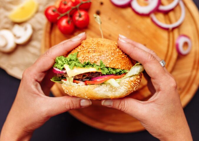 Photo shows a woman's hands holding a mushroom burger with a wooden chopping board and ingredients in the background. A new study has found that generative AI can help create more delicious, sustainable, and nutritious burgers, including plant-based options.
