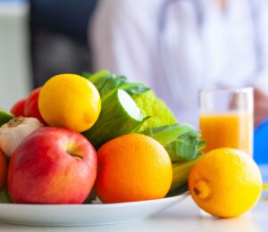 Photo shows a large bowl of fresh fruit and vegetables on a table, as someone in a lab coat writes on a clip board. Dr Mathew Nagra has debunked claims that Bryan Johnson’s recent diagnosis of autoimmune gastritis (AIG) was caused by a vegan diet
