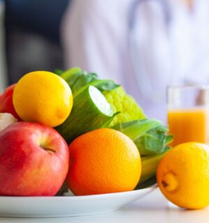 Photo shows a large bowl of fresh fruit and vegetables on a table, as someone in a lab coat writes on a clip board. Dr Mathew Nagra has debunked claims that Bryan Johnson’s recent diagnosis of autoimmune gastritis (AIG) was caused by a vegan diet