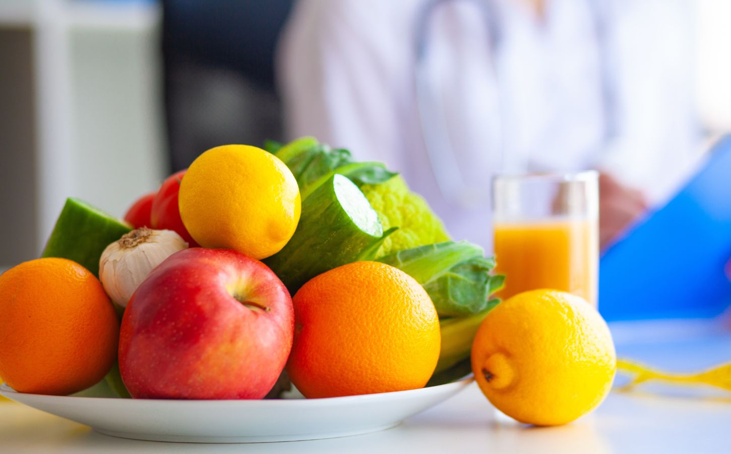 Photo shows a large bowl of fresh fruit and vegetables on a table, as someone in a lab coat writes on a clip board. Dr Mathew Nagra has debunked claims that Bryan Johnson’s recent diagnosis of autoimmune gastritis (AIG) was caused by a vegan diet