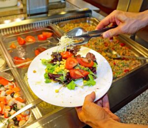 Photo shows a man putting fresh salad and vegetables on a plate in front of a buffet. The European Court of Human Rights (ECHR) has found that Switzerland violated two vegan prisoners’ “freedom of conscience” when it failed to provide them with meals consistent with their ethical beliefs
