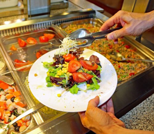 Photo shows a man putting fresh salad and vegetables on a plate in front of a buffet. The European Court of Human Rights (ECHR) has found that Switzerland violated two vegan prisoners’ “freedom of conscience” when it failed to provide them with meals consistent with their ethical beliefs
