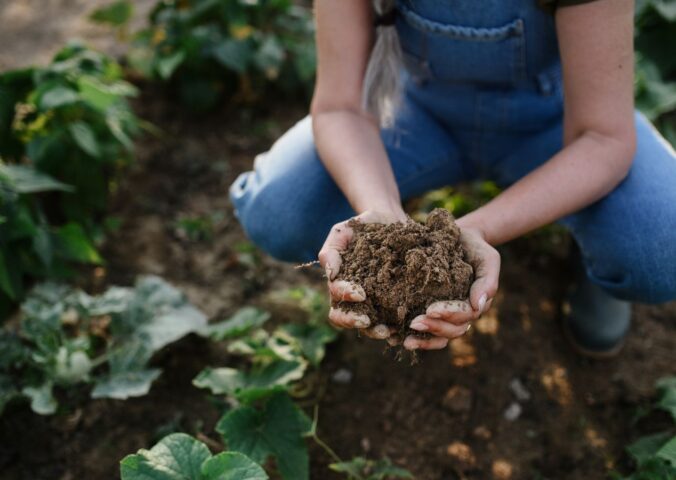 Photo shows a woman in overalls bending down and holding a handful of soil. New research has found a widening “credibility gap” between the regenerative farming claims made by the world’s biggest food companies and reality