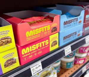 Photo shows boxes of Misfits protein bars on a shelf in the US, many of which use the phrase "plant-powered." Misfits Health has announced a new protein bar made with dairy chocolate, whey powder, and bovine collagen, and its vegan customers are not happy