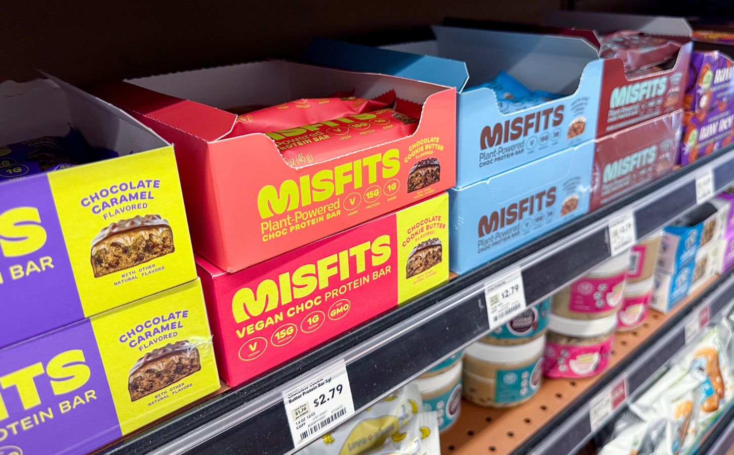 Photo shows boxes of Misfits protein bars on a shelf in the US, many of which use the phrase "plant-powered." Misfits Health has announced a new protein bar made with dairy chocolate, whey powder, and bovine collagen, and its vegan customers are not happy