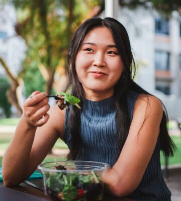 Photo shows a young woman eating lunch in front of her university building. A Peru court has ordered a major university to provide plant-based meals for its vegan student population