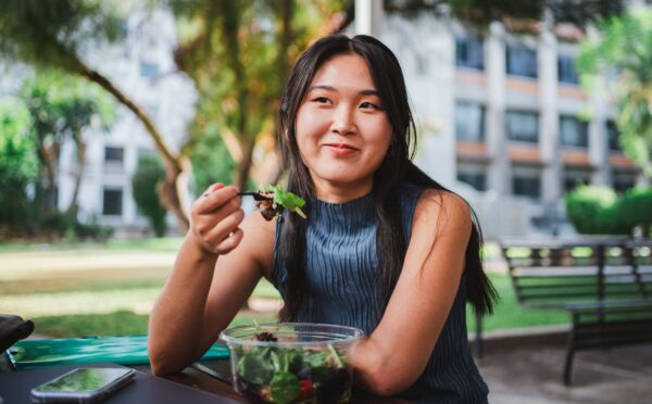 Photo shows a young woman eating lunch in front of her university building. A Peru court has ordered a major university to provide plant-based meals for its vegan student population