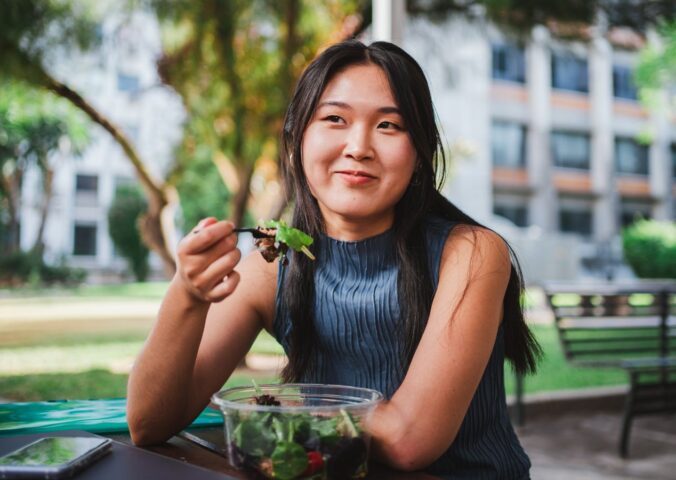 Photo shows a young woman eating lunch in front of her university building. A Peru court has ordered a major university to provide plant-based meals for its vegan student population