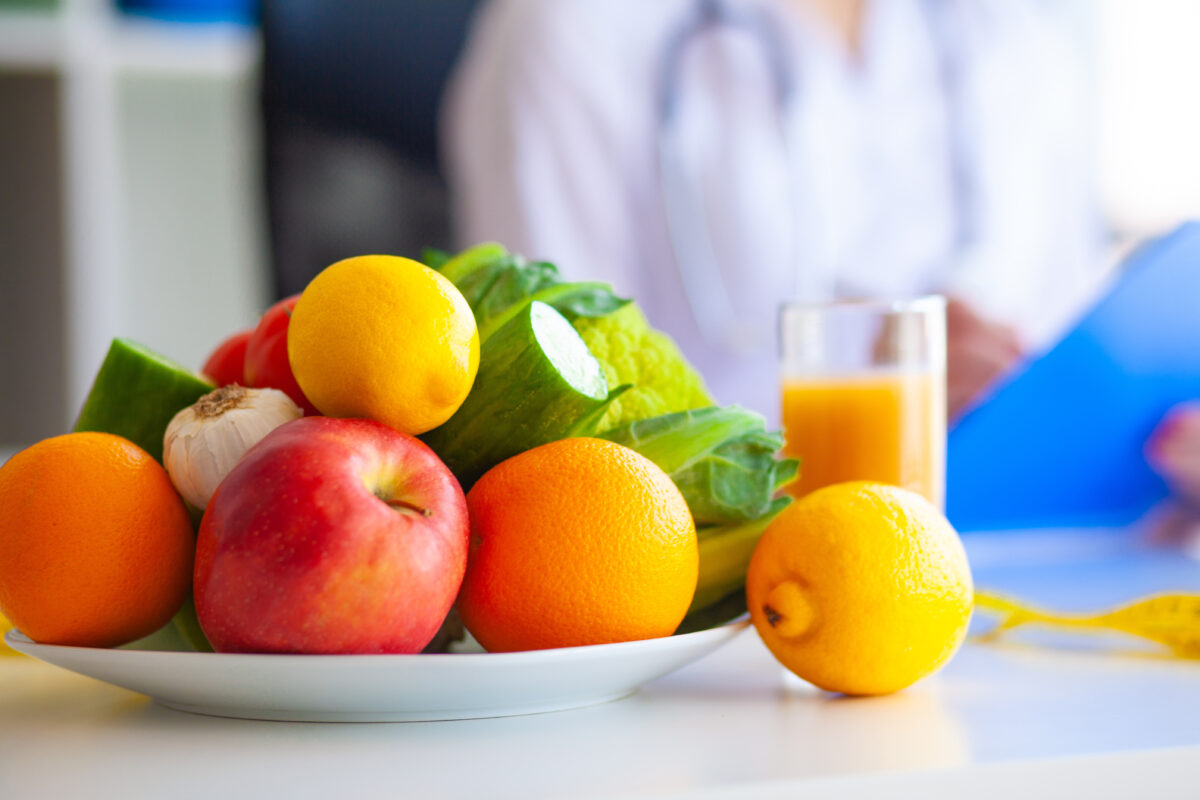 Photo shows a medical doctor writing on a clipboard next to a large bowl of fresh fruit and vegetables. Based on his new "Make Hospital Food Healthy Again Pledge," could RFK Jr be coming round to the idea of plant-based protein?