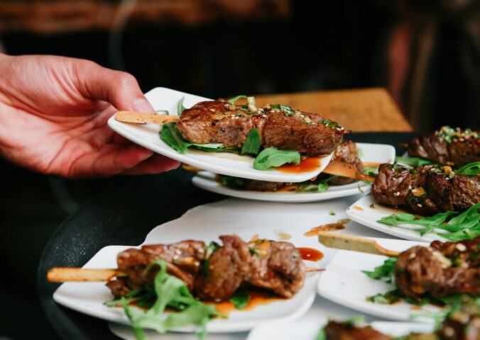Photo shows someone placing a plate of steak down on a table alongside several other plates. The UK has published fresh guidance for companies developing new cultivated meat proteins and other novel foods