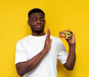 Photo of a man in front of a yellow background saying no to a burger, to illustrate article about a new study on what influences people to eat less meat