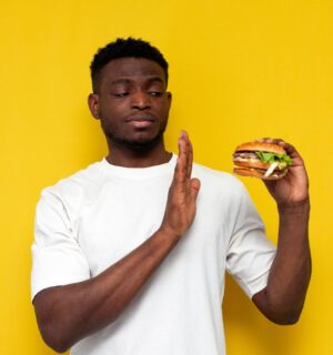 Photo of a man in front of a yellow background saying no to a burger, to illustrate article about a new study on what influences people to eat less meat