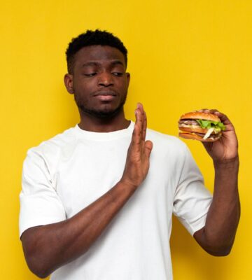 Photo of a man in front of a yellow background saying no to a burger, to illustrate article about a new study on what influences people to eat less meat