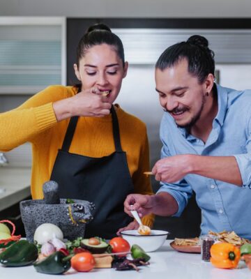 Couple eating chips and salsa surrounded by vegetables, illustrating the healthiest vegetables for men versus women
