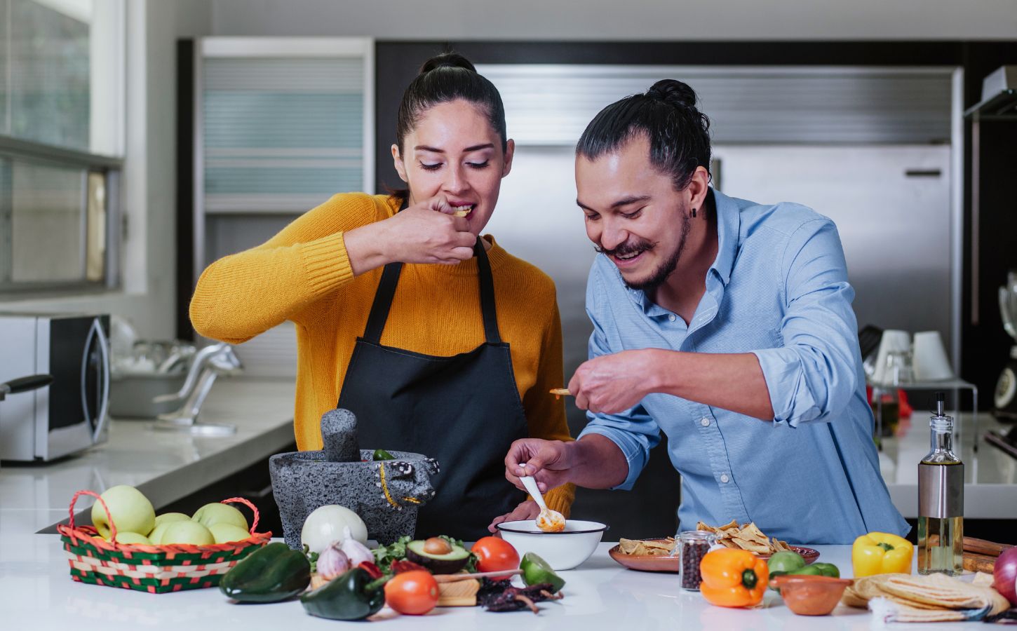 Couple eating chips and salsa surrounded by vegetables, illustrating the healthiest vegetables for men versus women