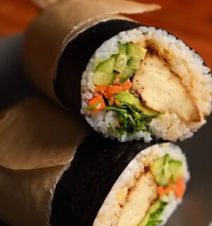 Image of the vegan sushi burrito wrapped in parchment paper and sitting on a plate, all ready to eat