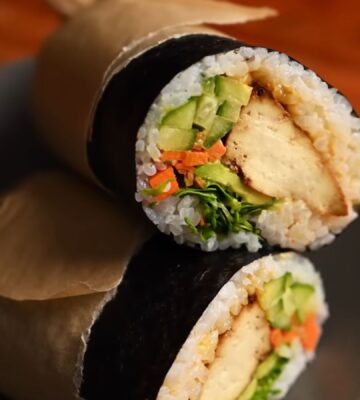 Image of the vegan sushi burrito wrapped in parchment paper and sitting on a plate, all ready to eat