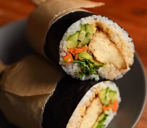 Image of the vegan sushi burrito wrapped in parchment paper and sitting on a plate, all ready to eat