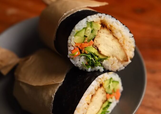 Image of the vegan sushi burrito wrapped in parchment paper and sitting on a plate, all ready to eat