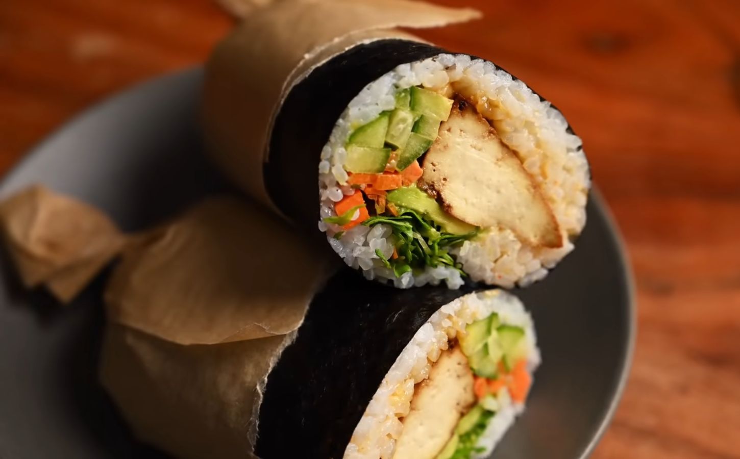 Image of the vegan sushi burrito wrapped in parchment paper and sitting on a plate, all ready to eat