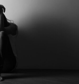 Black and white photo of a teenage girl sitting alone on the floor in a dark room, to illustrate the connection between gut and mental health