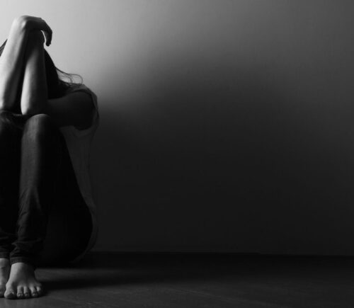 Black and white photo of a teenage girl sitting alone on the floor in a dark room, to illustrate the connection between gut and mental health