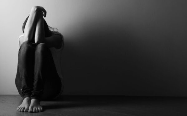 Black and white photo of a teenage girl sitting alone on the floor in a dark room, to illustrate the connection between gut and mental health