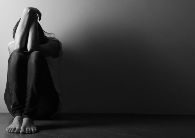 Black and white photo of a teenage girl sitting alone on the floor in a dark room, to illustrate the connection between gut and mental health