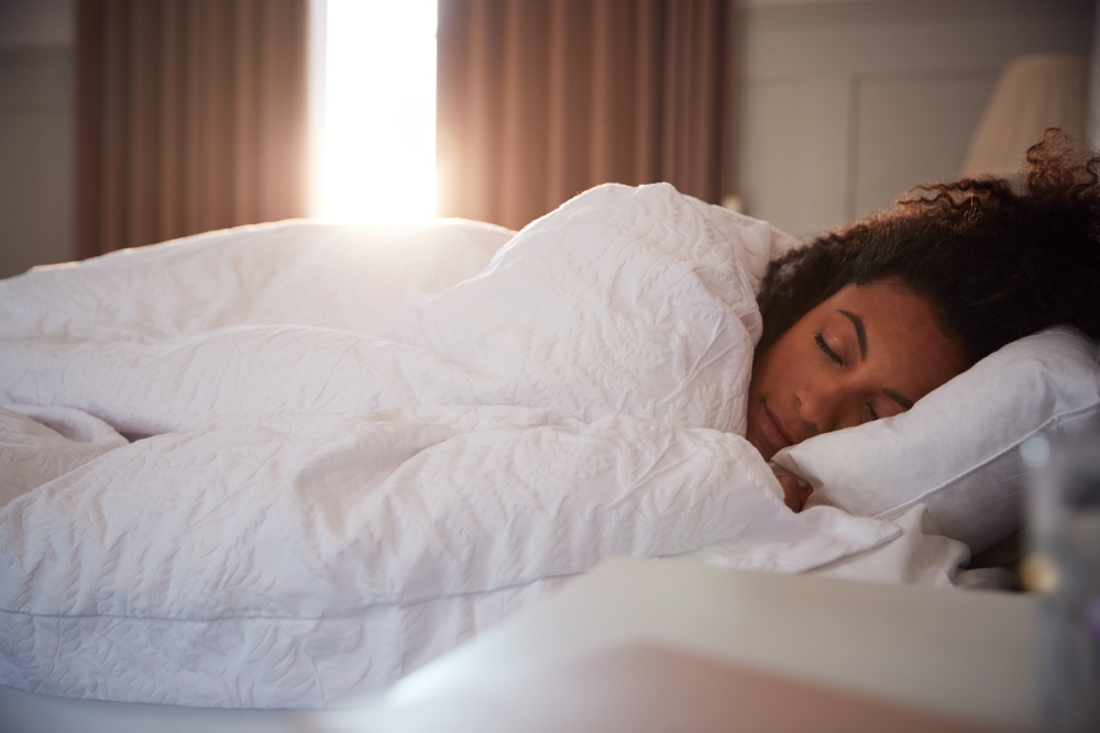 Photo of a woman sleeping under a white duvet in bed, to illustrate the connection between gut and mental health