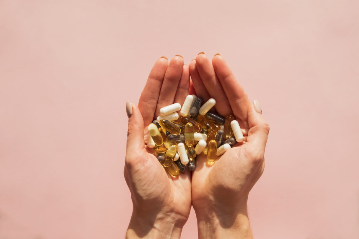 Photo shows a woman's hands holding many different vitamins and dietary supplements