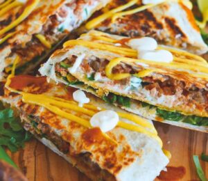 crunchy tostada wrap with corn tortilla, lentils, refired beans, vegan cheese sauce, cashew sour cream and more