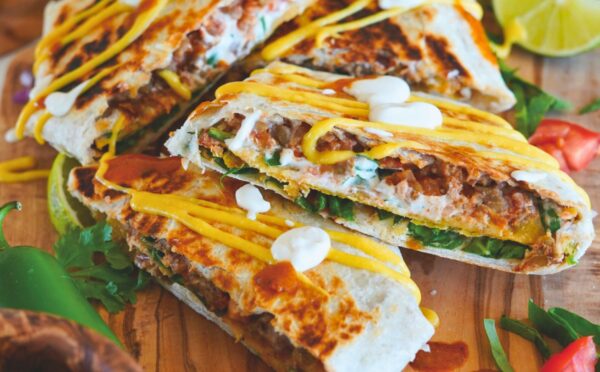 crunchy tostada wrap with corn tortilla, lentils, refired beans, vegan cheese sauce, cashew sour cream and more