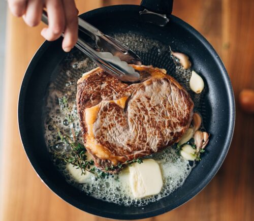 Photo shows someone cooking a steak in a cast iron pan with a lot of butter. PCRM, an American doctors’ group, has filed a lawsuit over the “industry-influenced” US dietary guidelines
