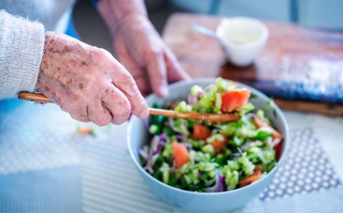 Photo shows an older woman's hands as she stirs a fresh salad in a bowl. A new study has examined what the children of centenarians eat.