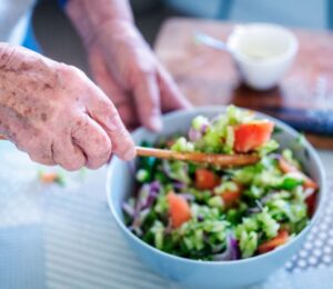 Photo shows an older woman's hands as she stirs a fresh salad in a bowl. A new study has examined what the children of centenarians eat.