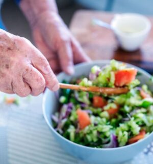 Photo shows an older woman's hands as she stirs a fresh salad in a bowl. A new study has examined what the children of centenarians eat.