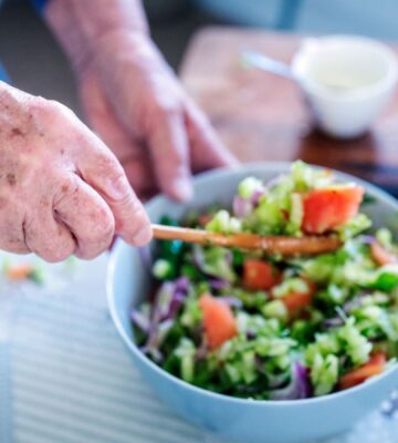 Photo shows an older woman's hands as she stirs a fresh salad in a bowl. A new study has examined what the children of centenarians eat.