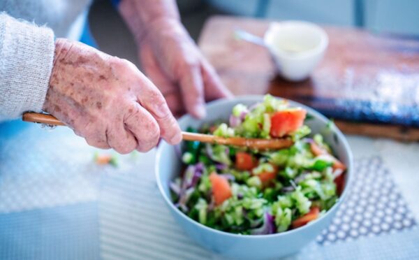 Photo shows an older woman's hands as she stirs a fresh salad in a bowl. A new study has examined what the children of centenarians eat.