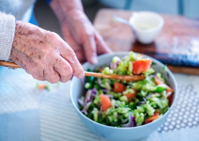 Photo shows an older woman's hands as she stirs a fresh salad in a bowl. A new study has examined what the children of centenarians eat.