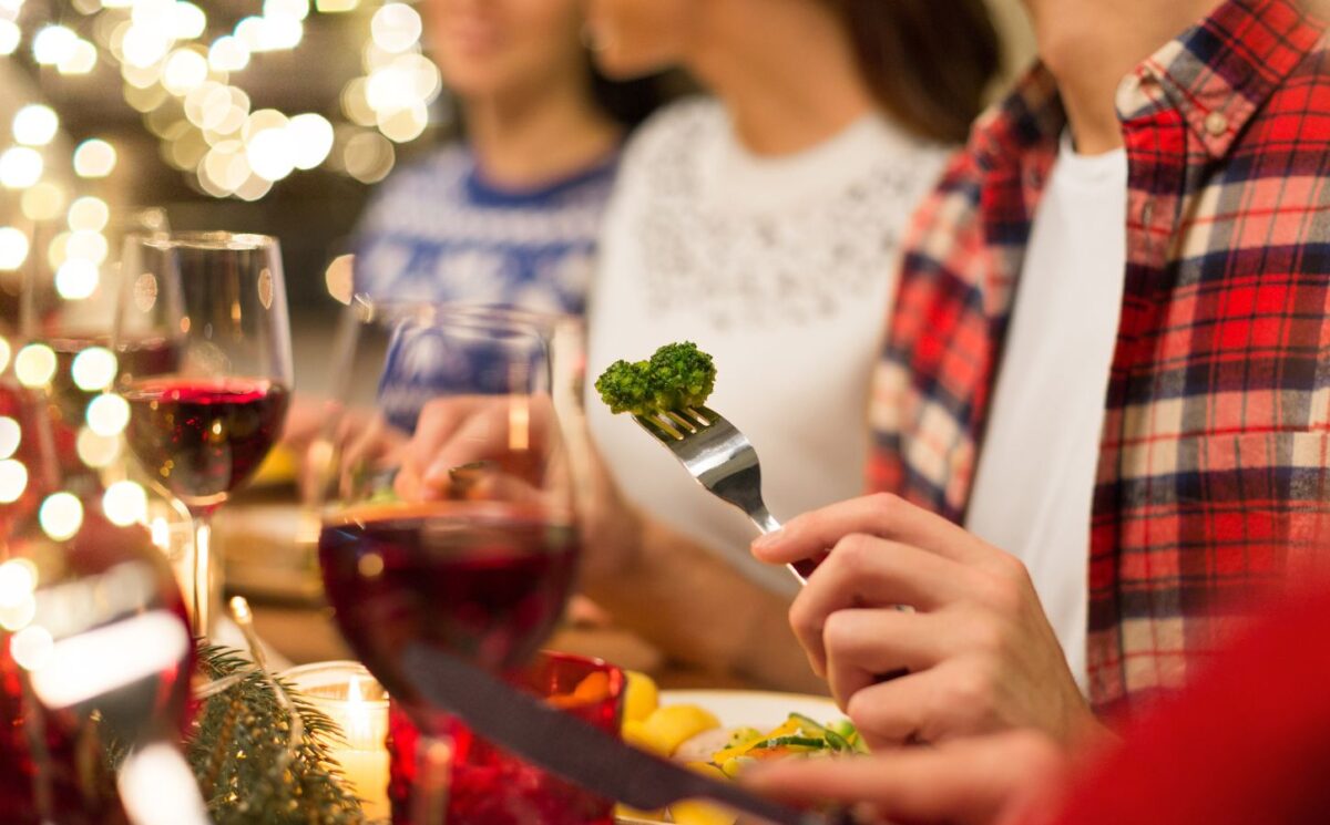 Photo shows three people eating vegetables and other meat-free options surrounded by festive lights. Nostalgia is a “major barrier” to dietary changes, including widespread adoption of plant-based diets, according to new research