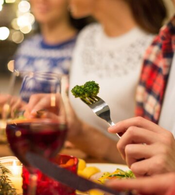 Photo shows three people eating vegetables and other meat-free options surrounded by festive lights. Nostalgia is a “major barrier” to dietary changes, including widespread adoption of plant-based diets, according to new research
