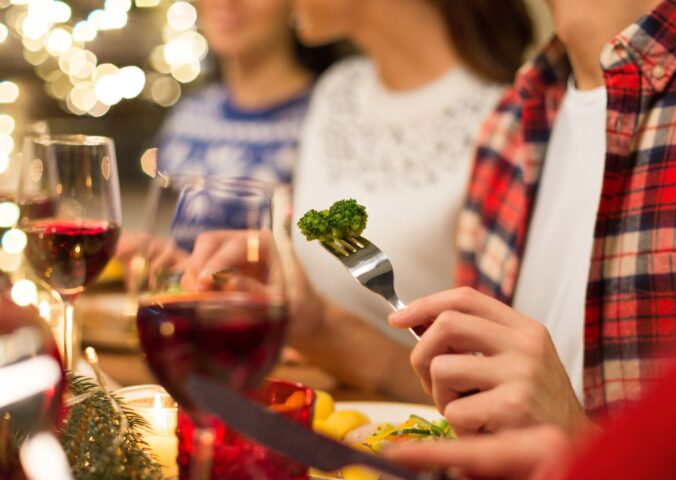 Photo shows three people eating vegetables and other meat-free options surrounded by festive lights. Nostalgia is a “major barrier” to dietary changes, including widespread adoption of plant-based diets, according to new research