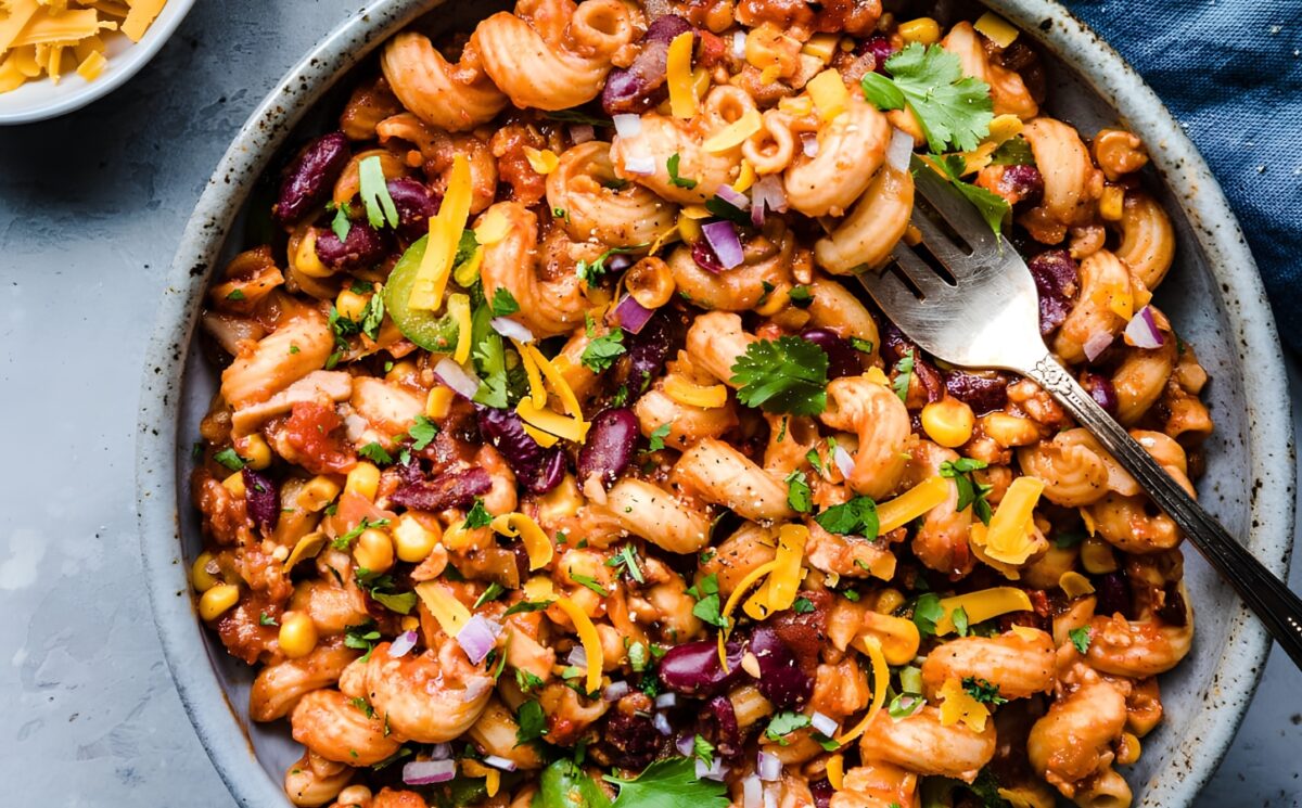 A vegan chili mac in a bowl next to dairy-free cheese and cilantro for basic vegan meals