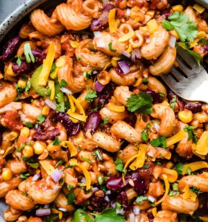 A vegan chili mac in a bowl next to dairy-free cheese and cilantro for basic vegan meals