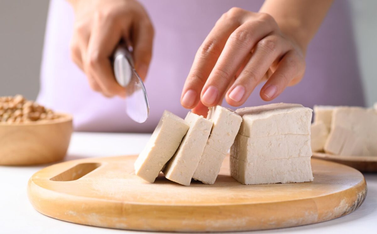 Photo shows someone cutting up a block of tofu. According to a scientist’s new scoring system, tofu is the single best protein for nutrition, sustainability, and affordability